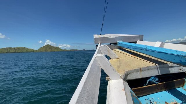 Komodo Islands, Indonesia: View from the prow of a blue and white wooden boat floating in tropical waters near Komodo National Park, with rugged islands on the horizon.