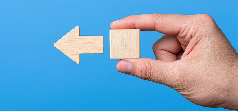 Hand flipping a wooden arrow block to point left, symbolizing new choices, changing direction, and innovative business decision-making.