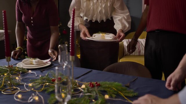 Woman placing festive plate on dining table beside multiethnic friends. Ideal for holiday lifestyle commercials and seasonal family dinner marketing campaigns