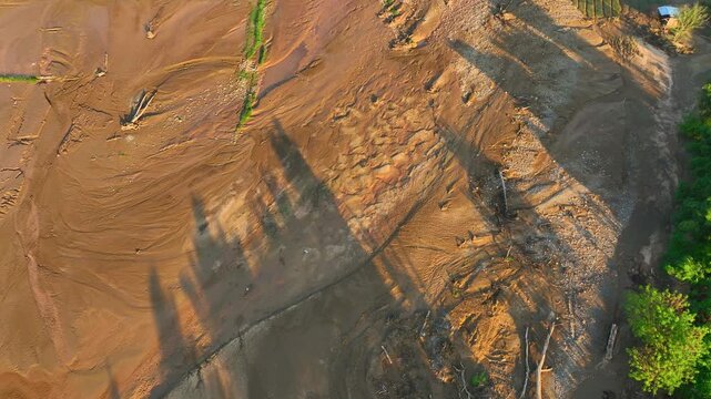 Aerial view captures widespread mud deposits and damaged field boundaries following flash flooding, revealing severe soil erosion, agricultural disruption, disaster recovery challenges. Nan, Thailand.