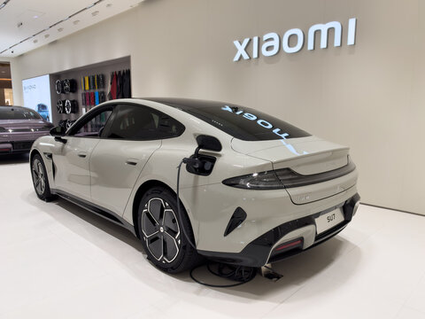Shenzhen, China - September 21, 2026: Xiaomi SU7 sedan charging with cable beside XIAOMI sign