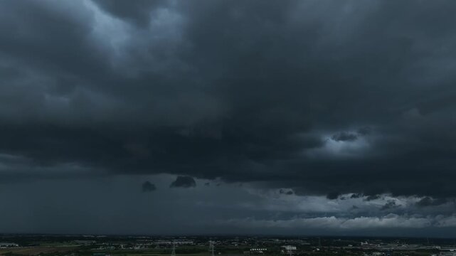 Aerial view captures dense layers of dark cumulonimbus clouds above distant buildings, emphasizing approaching heavy rain, thunderstorm development, extreme weather, and atmospheric instability. 4k.

