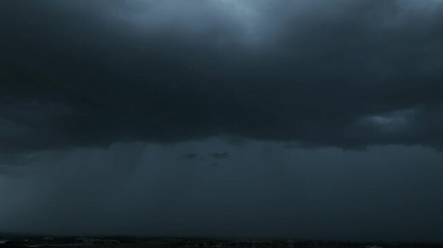 Aerial view captures dramatic black rain clouds gathering above an urban landscape, revealing an approaching tropical storm, heavy precipitation, changing weather patterns, and atmospheric turbulence.