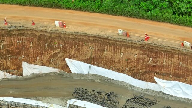A damaged roadside foundation following a major landslide, illustrating ground displacement, steep slope erosion, construction barriers, and disaster mitigation measures. Phrae Province, Thailand.