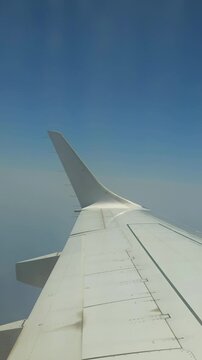 Close view of a commercial airplane wing against a clear blue sky, filmed from a passenger window during air travel.