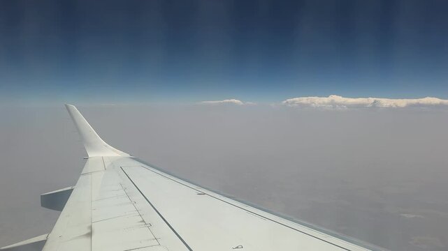 View of an airplane wing extending above a thick layer of clouds under a blue sky during a flight.