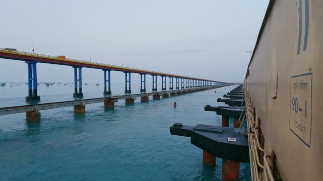 POV video from a moving train crossing Pamban Railway Bridge near Rameswaram, Tamil Nadu, India, showcasing the railway tracks, turquoise seawater, and parallel bridge structure along the coast.