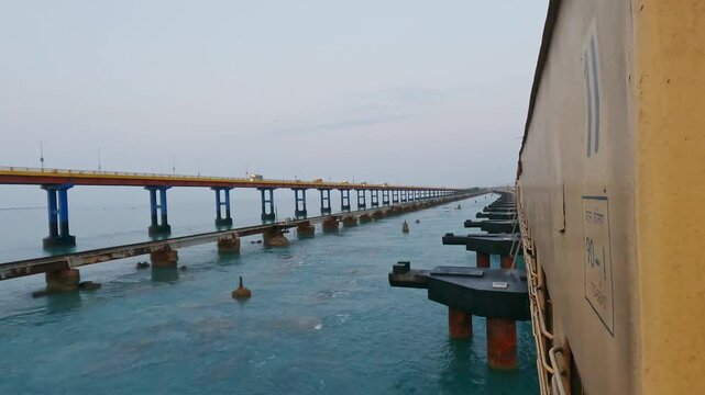 POV video from a moving train crossing Pamban Railway Bridge near Rameswaram, Tamil Nadu, India, showcasing the railway tracks, turquoise seawater, and parallel bridge structure along the coast.