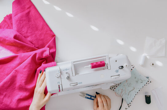 Overhead view of sewing machine with magenta linen fabric and tools on white surface