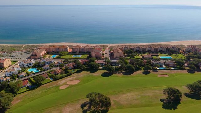 Incredible aerial backward movement over a lush green golf course revealing the stunning mediterranean coastline, with sandy beaches and holiday resorts on a sunny day in pals, girona, spain