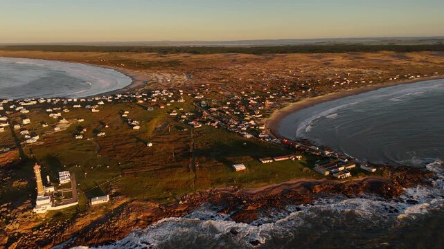 Remote coastal village and historic lighthouse on the rocky peninsula of Cabo Polonio at sunset in Rocha, Uruguay. Aerial drone panoramic view