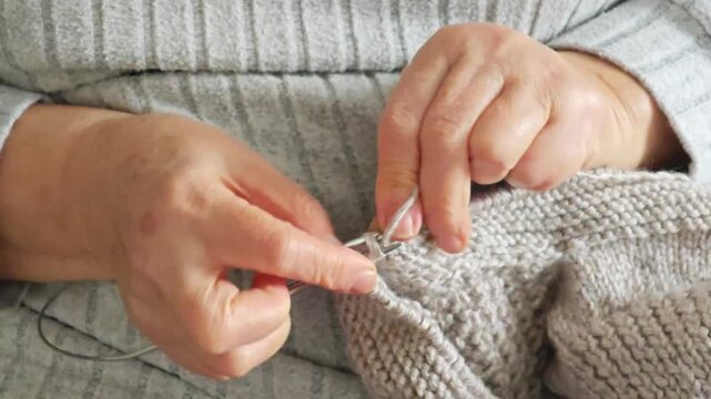 Close up of elderly woman hands knitting woolen clothes with needles Perfect for marketing campaigns regarding cozy home lifestyle crafts or senior hobbies