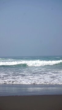Wide coastal landscape of Parangtritis Beach featuring foaming ocean waves and sprawling dark sand under a clear blue sky.