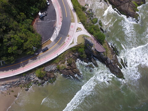 Top down aerial view of coastal road, viewpoint deck and waves crashing on rocks in Itajai, Santa Catarina, Brazil
