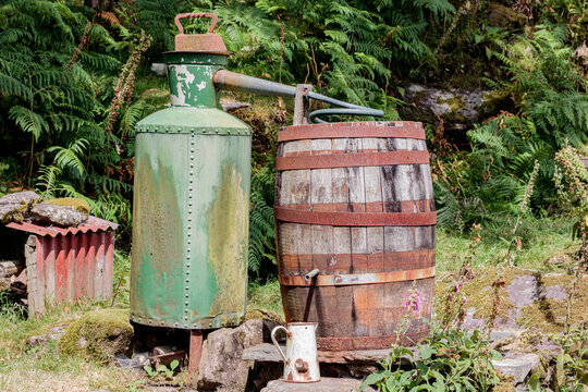Traditional vintage moonshine still with green copper pot and wooden barrel setup in rural outdoor forest setting