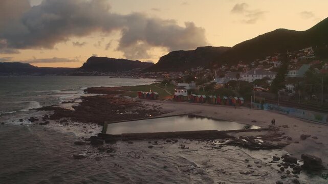 Aerial drone view of a scenic coastal town with a tidal pool and rocky shoreline at sunset with warm dramatic light