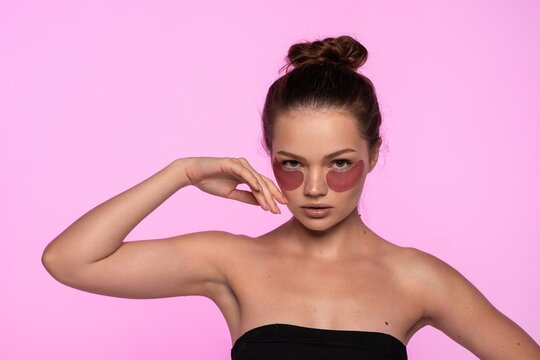 Young woman wearing eye patches achieving beauty and wellness while relaxing on a pink background