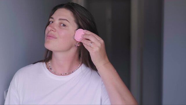 Woman using pink microcurrent device for forehead lifting. Professional anti-aging skincare routine and facial massage at home. Modern beauty tech for glowing skin.