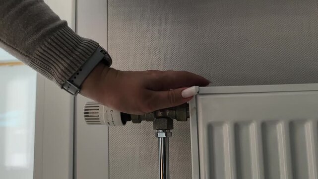 Heating crisis temperature adjustment amidst a heat shortage. High cost of electricity. A woman turns a thermostat dial. Heating season, turning on the heat, cold weather, energy saving.
