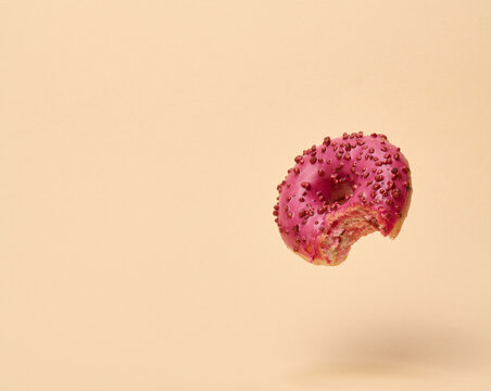 Single levitating bitten pink donut with glaze and berry sprinkles