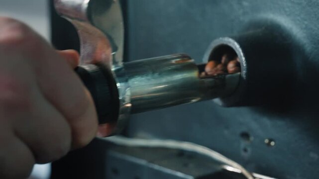 Male worker hand operating lever on coffee roaster machine at production facility opening metal chute and releasing beans for mixing blending roasting beverage preparation making caffeine food indoor