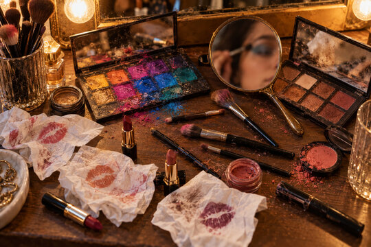Cluttered makeup vanity with colorful palettes used brushes and lipstick stained tissues