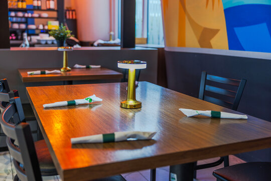 Close-up view of wooden restaurant table set with wrapped cutlery and illuminated table lamp. Miami Beach. USA.