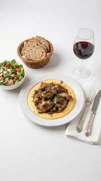 Rabbit stew with creamy polenta, mushroom sauce, fresh salad, artisan bread, and a glass of red wine on a set table
