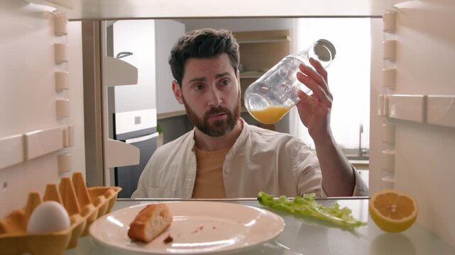Confused Caucasian hungry man opening empty refrigerator eating crumbs needing food products POV inside fridge male guy with lemon lettuce egg bread juice bottle ordering delivery problem solution