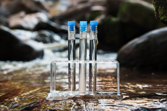 A clear plastic test tube rack holding three test tubes with blue caps placed in a flowing stream.