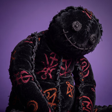 Halloween voodoo doll sculpted from densely compressed black velvet fibers with crooked limbs, crimson and orange textile patterns, button eyes and stitched facial details.
