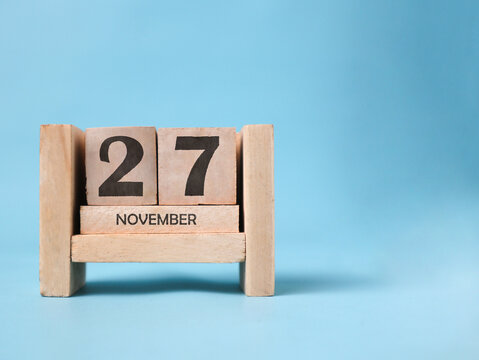 A wooden block calendar for November 27th on a light blue background.