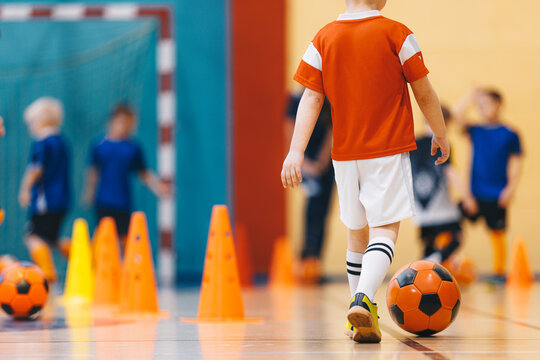 Junior Futsal Player in Orange Shirt Dribbling Ball Past Orange Training Cones - Indoor Soccer Practice Session in Gymnasium