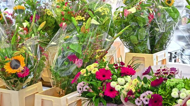A close-up shot of various colorful flower bouquets wrapped in transparent plastic, displayed in buckets and crates at a flower market or shop.