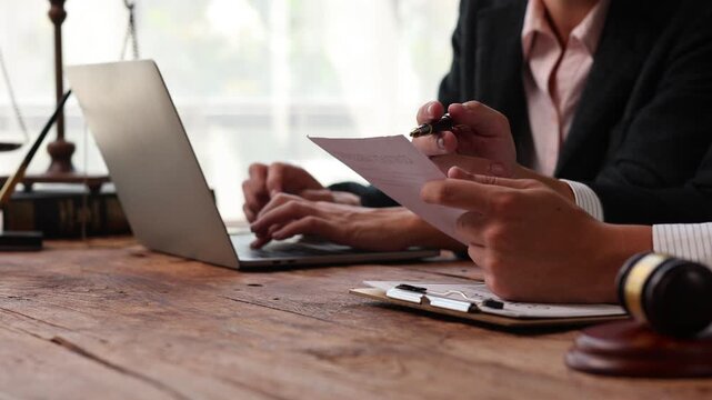 Lawyers consulting and discussing a contract while typing on a laptop at a law firm office with a gavel on the table