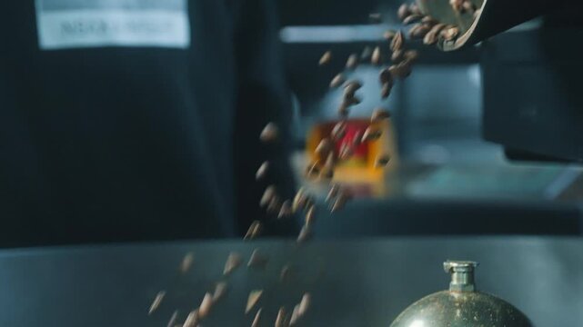 Brown roasted coffee beans cascading from a modern steel roaster close up stream of grains falling through factory equipment during automated processing production drink beverage preparation inside