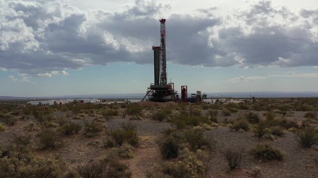 Red and white drilling rig operating at a shale gas field in Vaca Muerta, Neuqu&eacute;n. A drone flies at low altitude, approaching very slowly. 4K.