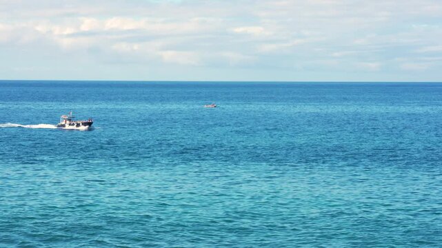A fast-moving speed boat cuts across the deep blue ocean under a clear, cloudless sky, leaving a long white trail of foam behind. The smooth water surface reflects sunlight as the vessel glides.
