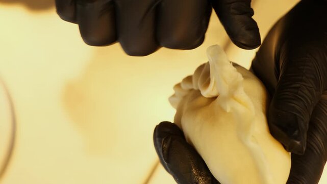 Gloved baker crimps dumpling edges into neat decorative braid by hand. Fingers pinch soft dough repeatedly creating secure patterned pastry seam