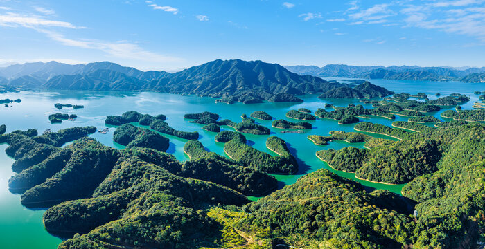 High angle view reveals forested green islands scattered across vibrant turquoise waters of Qiandao Lake in Zhejiang, China under clear blue skies.
