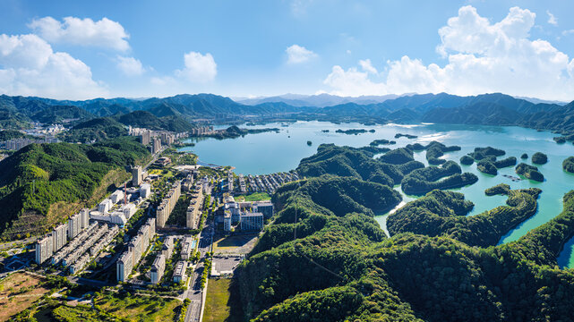High angle panoramic view of Qiandao Lake city in Zhejiang, China, featuring lush islands, clear water, and urban scenery under sunny sky.