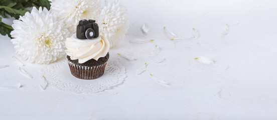 Cupcake decorated with a miniature chocolate camera with a bouquet of peonies. Holiday greetings concept, banner, background. Festive still life with selective focus and copy space for text © Nymphalyda
