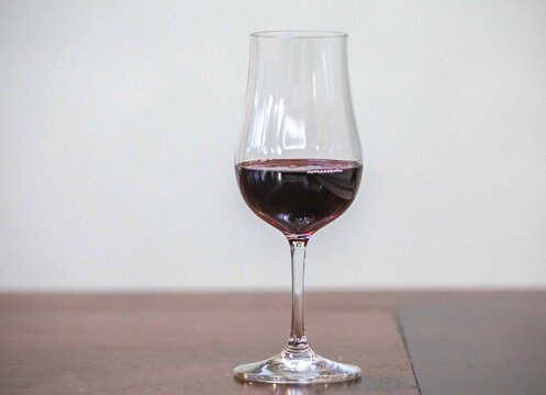 A glass of red wine on a dark wooden table against a textured grey concrete wall, with copy space &mdash; tulip-shaped tasting glass holding deep ruby wine in soft natural light.