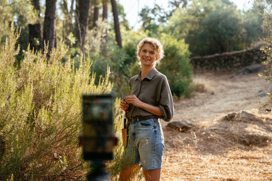 Cheerful mature plant expert creating social media content during rosemary harvest