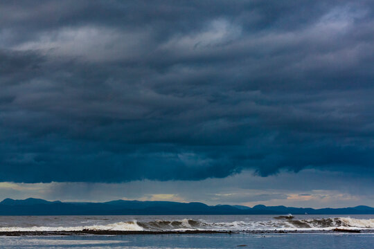 A line of waves breaking into surf, the wilderness beach on the Strait of Juan de Fuca under a very stormy dark sky.