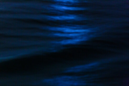 The ocean surface, midnight blue colours in the darkness, reflections and ripples on the water.