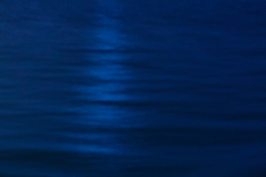 The ocean surface, midnight blue colours in the darkness, reflections, a faint shaft of light on the water.