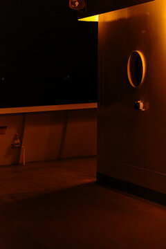 A round window in a wall, a boat deck in darkness with a sliver of light reflection.