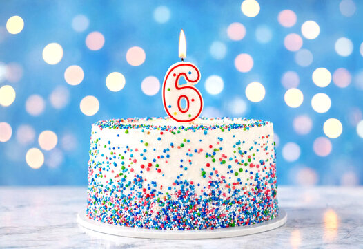 Colorful sprinkle birthday cake with lit candle number six