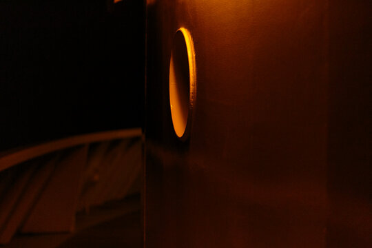 A round window in a wall, a boat deck in darkness with a sliver of light reflection.